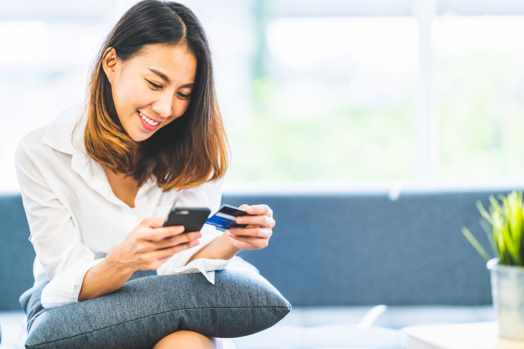 young-asian-woman-using-credit-card-to-pay-via-mobile-at-home